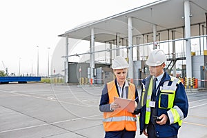 Male and female workers discussing over clipboard in shipping yard