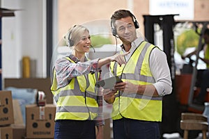 Male And Female Workers Wearing Headsets In Logistics Distribution Warehouse Using Digital Tablet