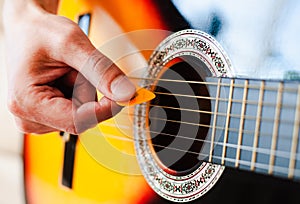 Male fingers with mediator playing on guitar strings. Close-up