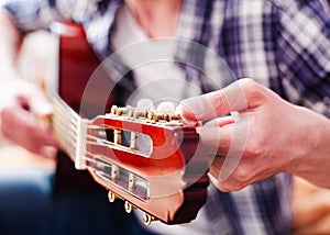 Male fingers tuning acoustic guitar. Close-up.