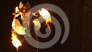 Male fire tamer in a thrilling close up fire show in a dark studio in the rain. A silhouette of a man swinging fiery