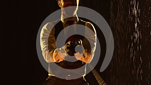 Male fire tamer in a thrilling close up fire show in a dark studio in the rain. A silhouette of a man swinging fiery