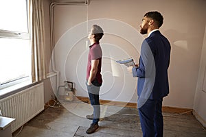 Male First Time Buyer Looking Around House For Renovation With Realtor