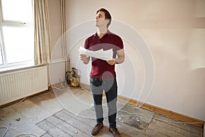 Male First Time Buyer Looking At House Survey In Room To Be Renovated