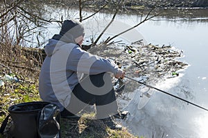A male fisherman catches fish in the spring with a fishing rod sitting on the Bank of the river. Sunny day, spring landscape.