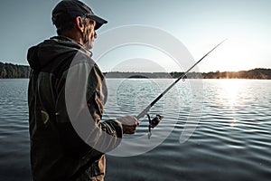 Male fisherman at dawn on the lake catches a fishing rod. Fishing hobby vacation concept. Copy space