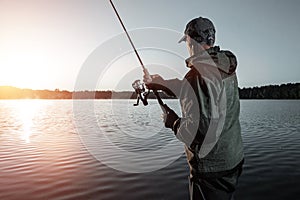 Male fisherman at dawn on the lake catches a fishing rod. Fishing hobby vacation concept. Copy space