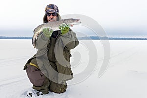 Male fisherman holding big fish Northern pike, and trophy. Winter fishing. Fishing in the winter