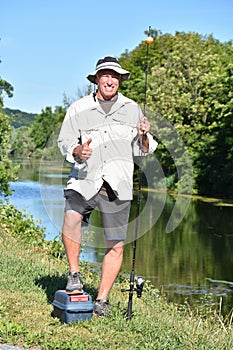 Male Fisherman With Thumbs Up With Rod And Reel Outdoors