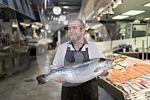 Male fishmonger wearing an apron holding large and whole salmon