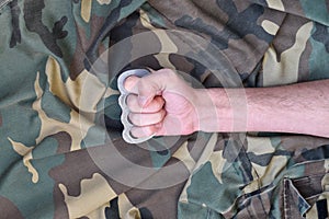 Male fist with brass knuckles on the background of a camouflage jacket. The concept of skinhead culture, handmade melee weapons