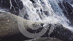 Male foot stepping on stone in flowing river from mountain waterfall. Male foot in shoe walking along rocky mountain