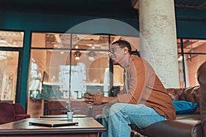 Smiling male freelancer in eyeglasses drinking coffee during break time in coworking