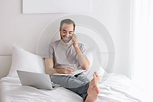 Male freelancer talking on phone while working in bed