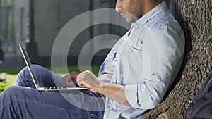 Male freelancer working on new project snugly locating in shadow of wide tree