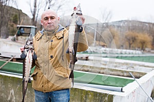 Male with fresh sturgeons in hands on farm outdoors