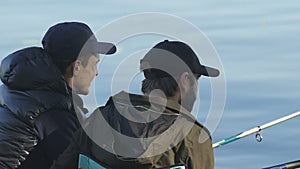 Male friends chatting enjoying process of angling, men trying to catch fish