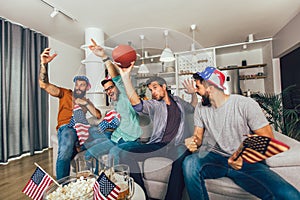 Male friends cheering while watching American football match on sofa at home