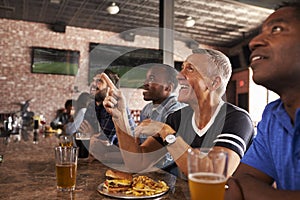 Male Friends At Counter In Sports Bar Watching Game