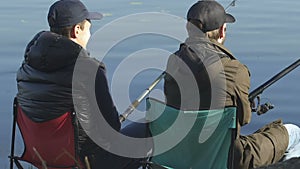 Male friends fishing, sitting on folding chairs, recreational activity outdoor