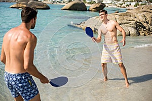 Male friends playing matkot on shore at beach