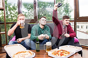 Male friends playing video games, drink beer and have fun at home