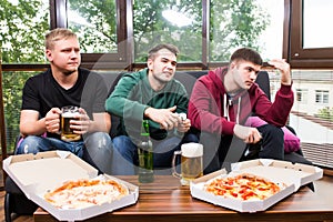 Male friends playing video games, drink beer and have fun at home