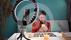 A male future predictor tells fortunes online using tarot cards while recording a live video for his blog