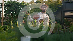 Male gardener with hose watering vegetable garden while his female colleague taking care of the plants