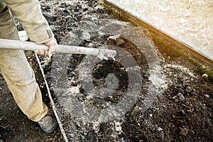 Male gardener worker digging in vegetable garden with shovel. Farmer man in rubber boots working hands with spade dig black soil,