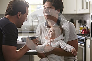 Male gay couple holding baby girl in their kitchen