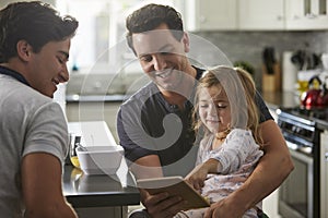 Male gay dads use tablet with daughter in kitchen, close up