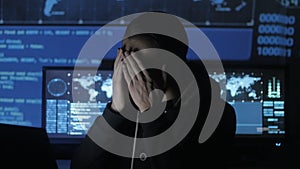 Male geek hacker overworking at computer and suffers from a headache in cyber security center filled with display