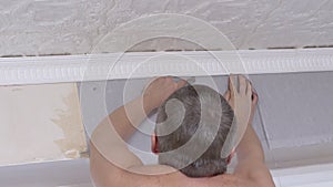 Male Glues Gray Paper Wallpaper on Wall under the Ceiling. Back view. 4K
