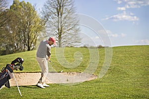 Male golf player pitching on course.