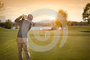 Male golf player swinging golf club at dusk.