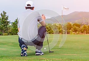 Male golfer kneeling holding golf club and checking path line