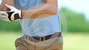 Male golfer making swing and feeling pain of cramp in elbow, starting massage