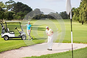 Male golfer playing on sand trap by woman
