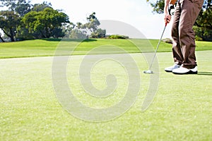 Male golfer putting the ball. Low section of golfer in position to putt the ball.