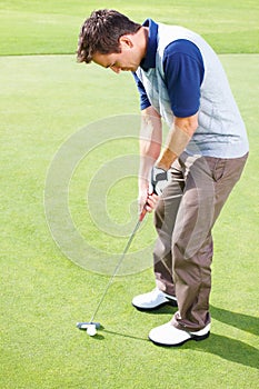 Male golfer ready to putt the ball. Male golfer standing on the putting green and taking his position to putt the ball.