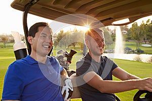 Male Golfers Driving Buggy Along Fairway Of Golf Course