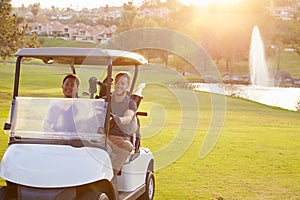 Male Golfers Driving Buggy Along Fairway Of Golf Course