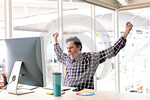 Male graphic designer celebrating success at desk in a modern office