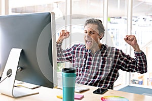 Male graphic designer celebrating success at desk in a modern office