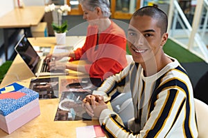 Male graphic designer looking at camera while coworker using laptop in the background