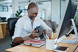 Male graphic designer reviewing captured images in his digital camera at desk