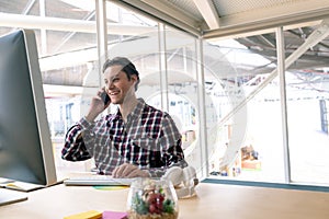 Male graphic designer talking on mobile phone at desk in a modern office