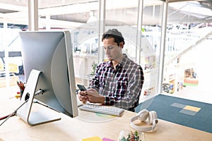 Male graphic designer using mobile phone at desk in a modern office