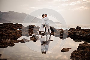 Male groom and female bride standing on the stone beach with the bouquet